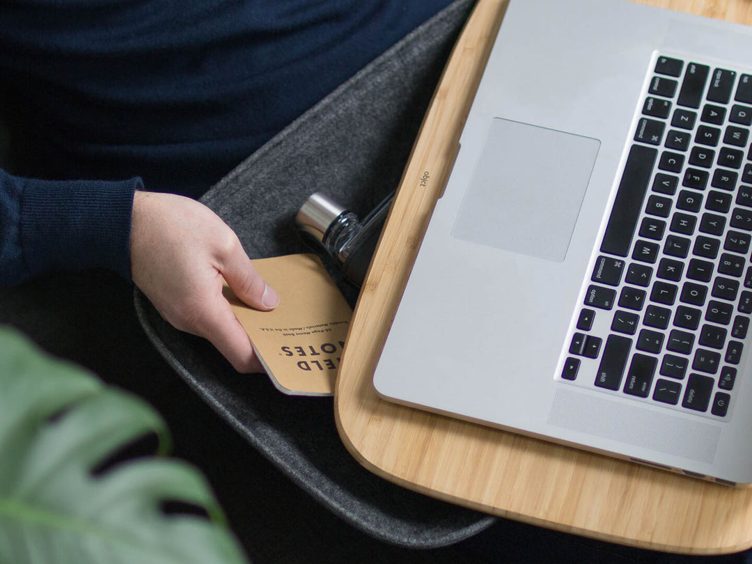 At home on a sofa couch working comfortably with a Macbook and Objct Lapod Lap Desk tech-organiser, in Ash Grey or Charcoal